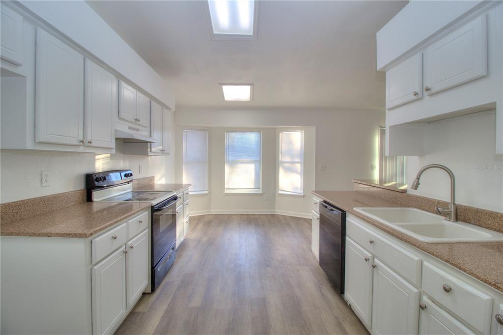 A kitchen with white cabinets, tan countertops, black appliances, and light wood-look flooring — 26 PECAN PASS TRAIL, OCALA, FL