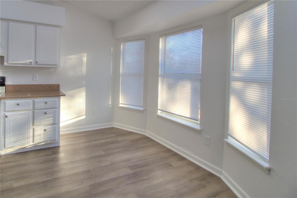 A bright kitchen nook features white cabinets, granite countertops, wood-look flooring, and three windows — 26 PECAN PASS TRAIL, OCALA, FL