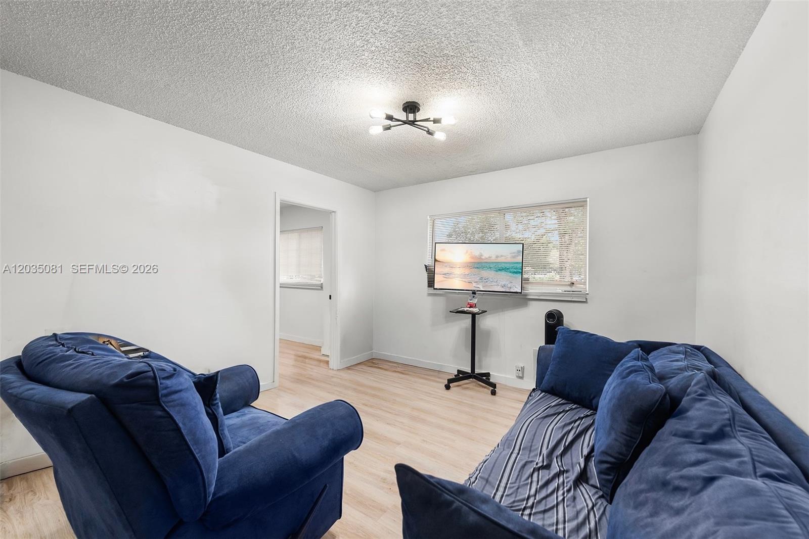 A living room features light wood flooring, white walls, blue sofas, and a television stand — 3700 N 56th Ave # 1012, Hollywood FL 33021, HOLLYWOOD, FL