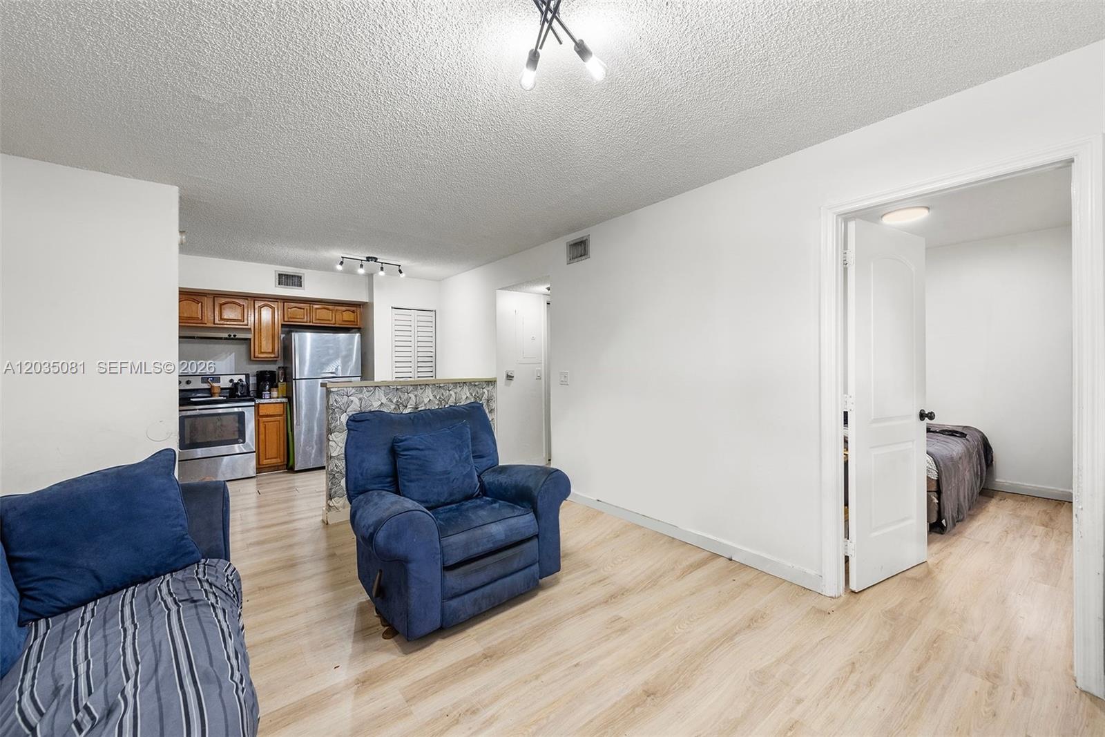 A living room with light wood flooring, a blue armchair, and an adjacent kitchen area — 3700 N 56th Ave # 1012, Hollywood FL 33021, HOLLYWOOD, FL