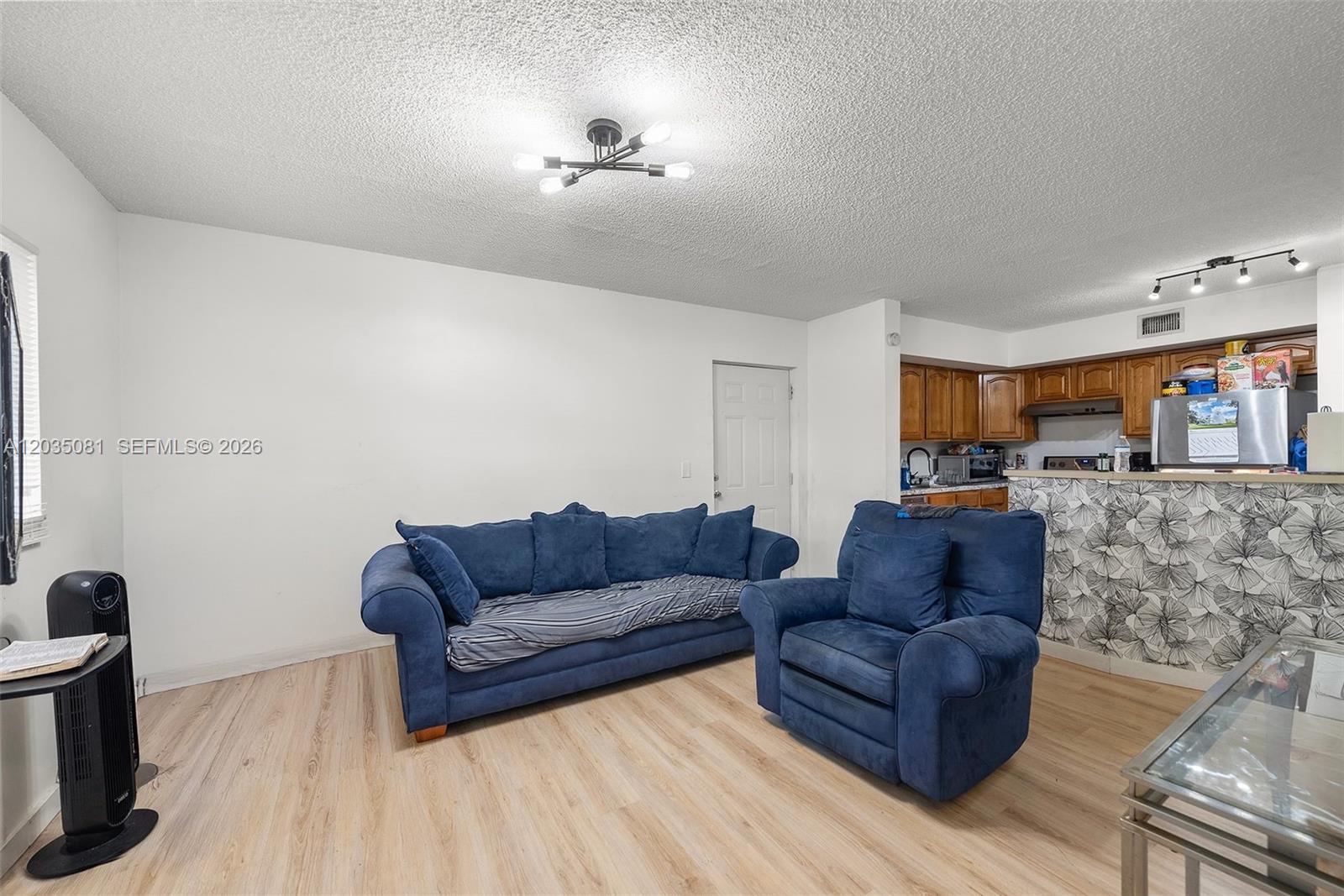 A living room features light wood-look flooring, blue upholstered furniture, and an open kitchen area — 3700 N 56th Ave # 1012, Hollywood FL 33021, HOLLYWOOD, FL