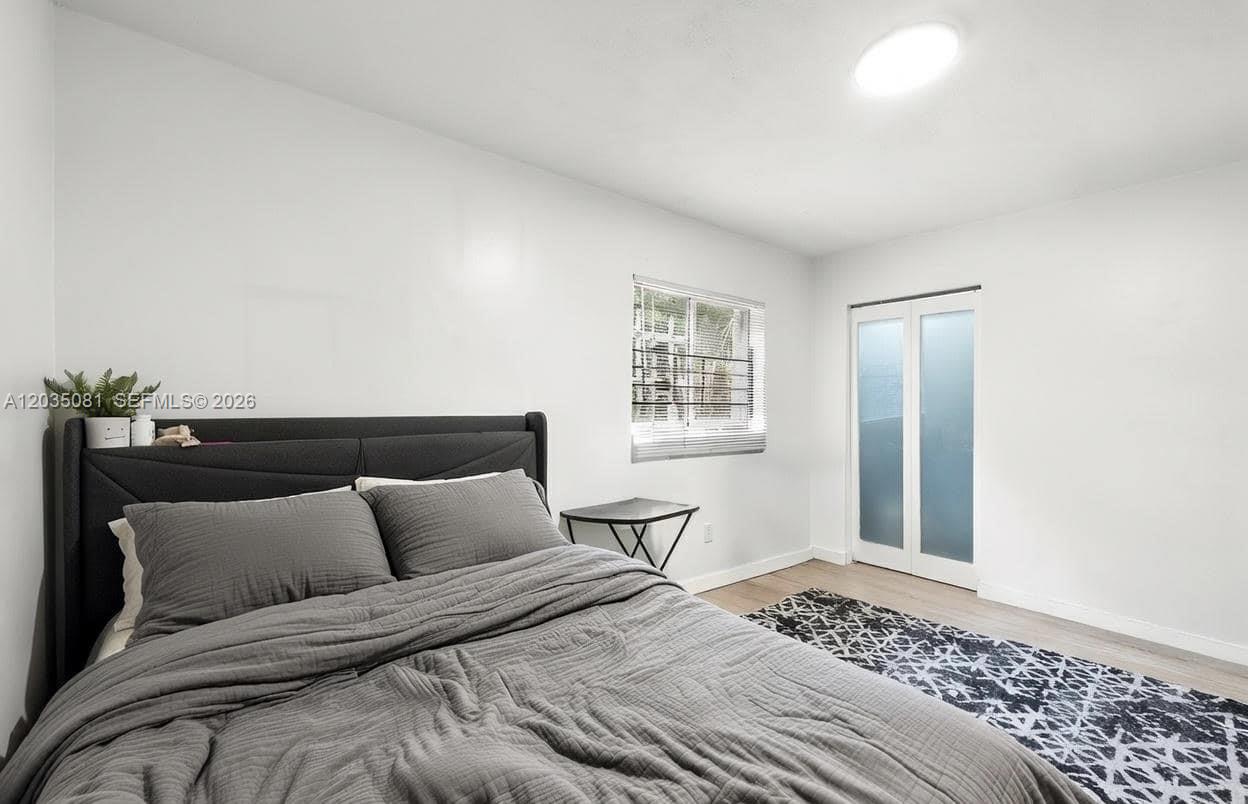 A bedroom features a gray upholstered bed, a small side table, and a window — 3700 N 56th Ave # 1012, Hollywood FL 33021, HOLLYWOOD, FL