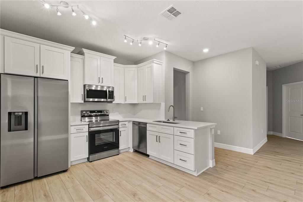 A modern kitchen features white cabinetry, stainless steel appliances, and light wood-look flooring — 3647 SUMMER HAVEN LANE, APOPKA, FL
