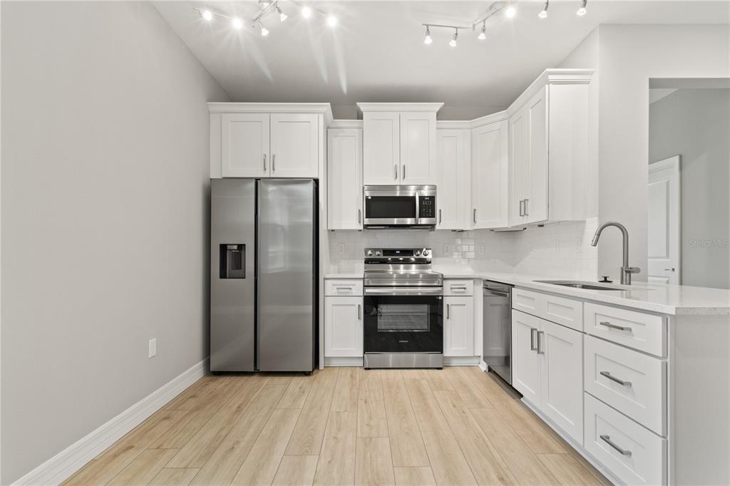 A modern kitchen features white cabinetry, stainless steel appliances, and light wood-look flooring — 3647 SUMMER HAVEN LANE, APOPKA, FL