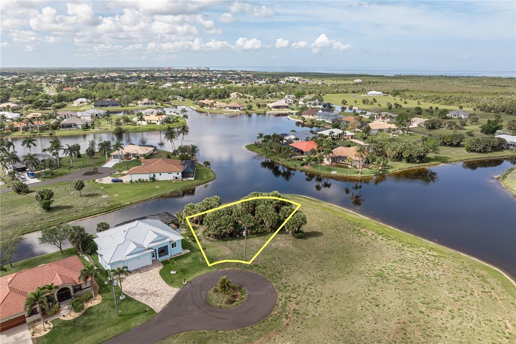 An aerial view shows a vacant, wooded residential lot outlined in yellow near a lake — 16396 NOGALES COURT, PUNTA GORDA, FL