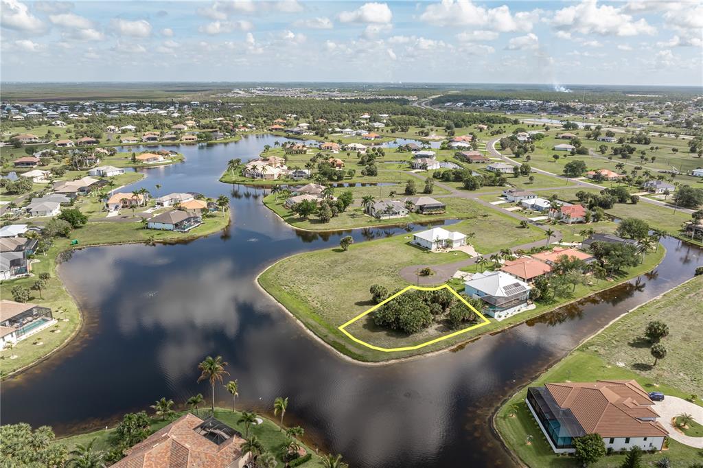 An aerial view shows a vacant waterfront lot outlined in yellow within a residential neighborhood — 16396 NOGALES COURT, PUNTA GORDA, FL