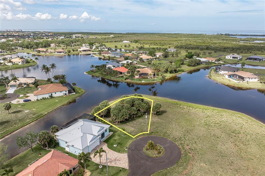 An aerial view shows a vacant, wooded residential lot outlined in yellow near a lake — 16396 NOGALES COURT, PUNTA GORDA, FL