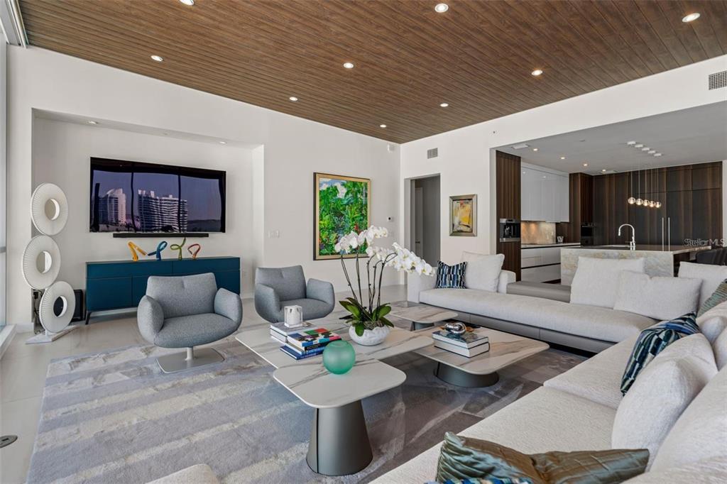 A modern living room features a wood-paneled ceiling, white walls, and an open-concept kitchen — 111 GOLDEN GATE POINT UNIT 802PH, SARASOTA, FL