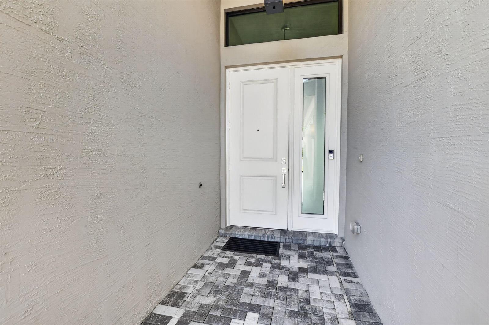 A front entryway features a white door with a glass sidelight and gray paver flooring — 17358 Santaluce Manor, Boca Raton FL 33496, BOCA RATON, FL