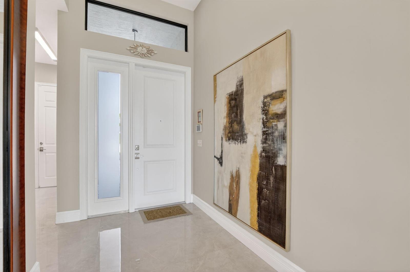 A bright entryway features a white front door, a large abstract painting, and tile flooring — 17358 Santaluce Manor, Boca Raton FL 33496, BOCA RATON, FL