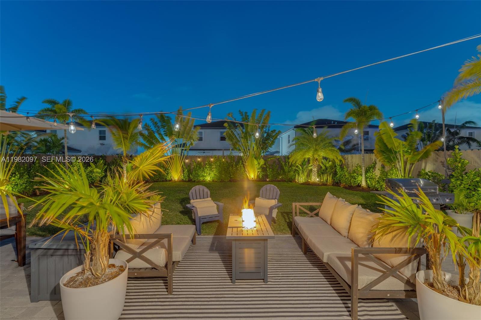 A backyard patio features a fire pit, outdoor seating, and string lights at dusk — 12741 SW 213th Ter, Miami FL 33177, MIAMI, FL