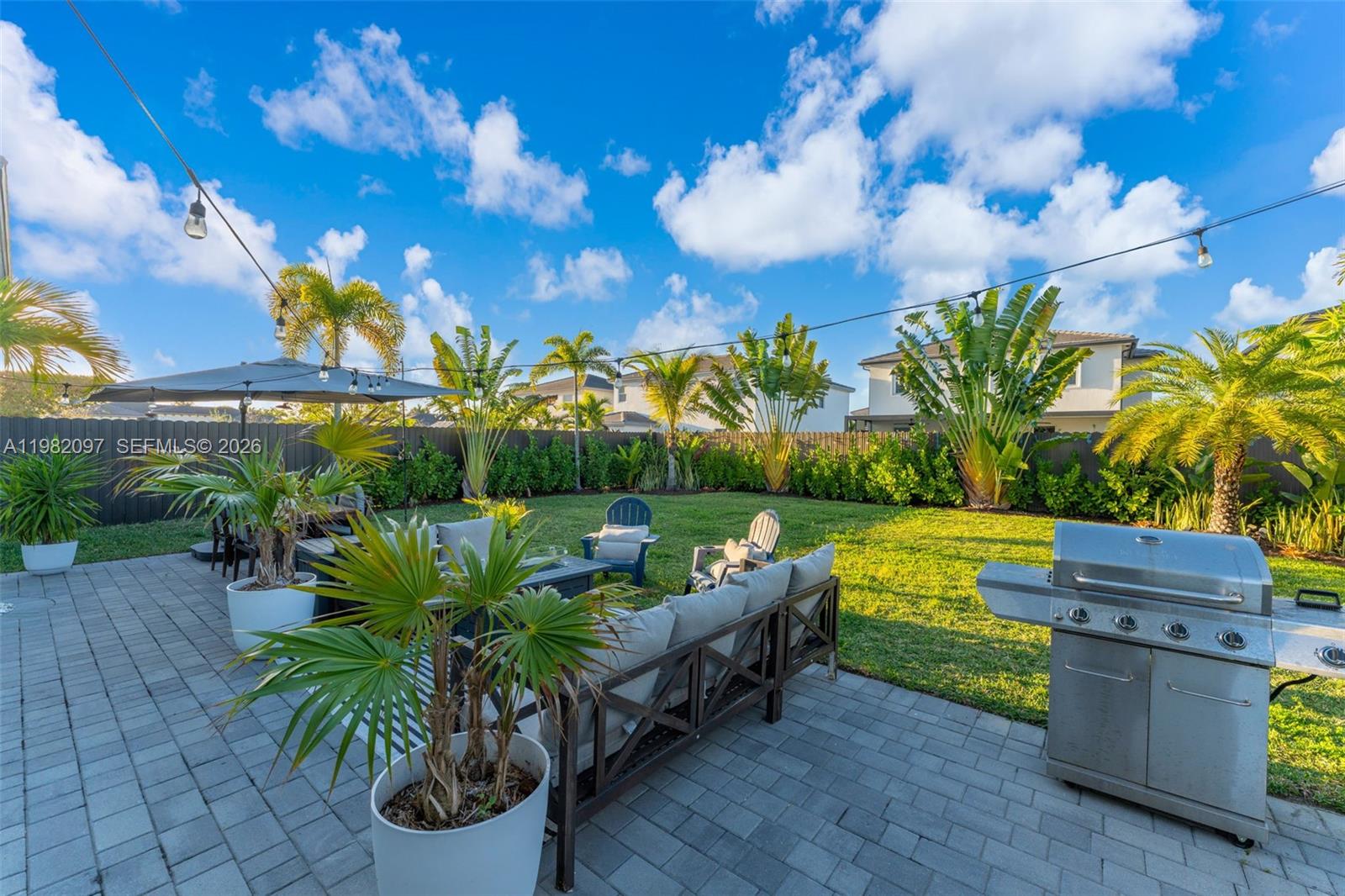 A paved backyard patio features outdoor furniture, a grill, and palm trees under a blue sky — 12741 SW 213th Ter, Miami FL 33177, MIAMI, FL