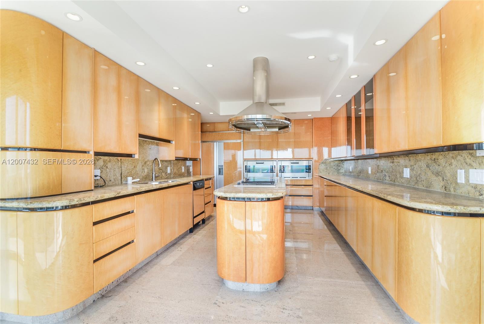A modern kitchen features light wood cabinetry, granite countertops, and a central island with a hood — 9601 Collins Ave # T4, Bal Harbour FL 33154, BAL HARBOUR, FL
