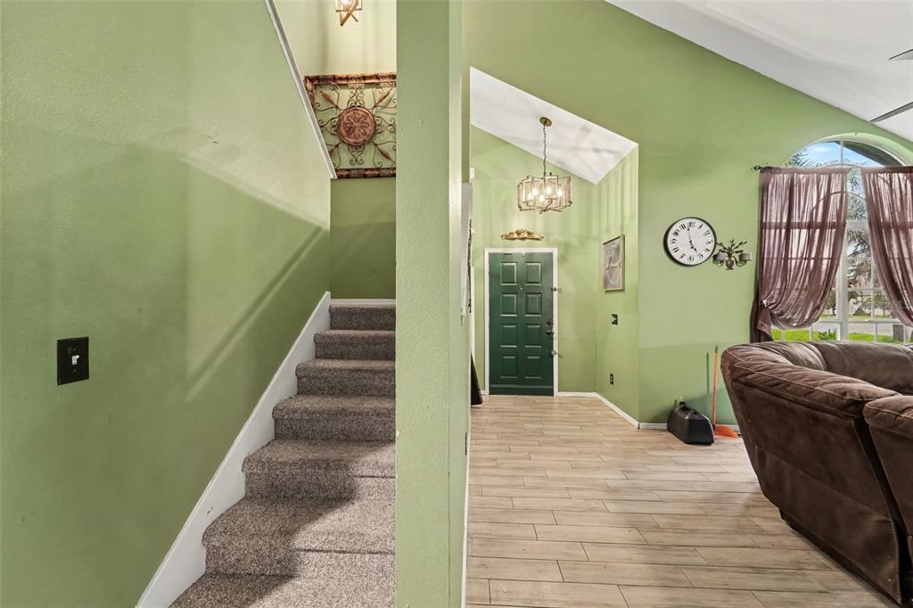 An entryway with green walls, a carpeted staircase, wood-look tile flooring, and a front door — 2405 ABALONE BOULEVARD, ORLANDO, FL