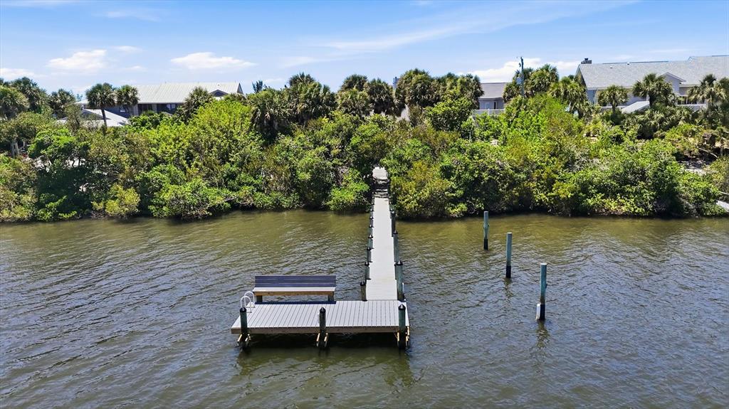 An aerial view shows a wooden dock extending from a lush, tree-lined shore into water — 750 N MANASOTA KEY ROAD, ENGLEWOOD, FL