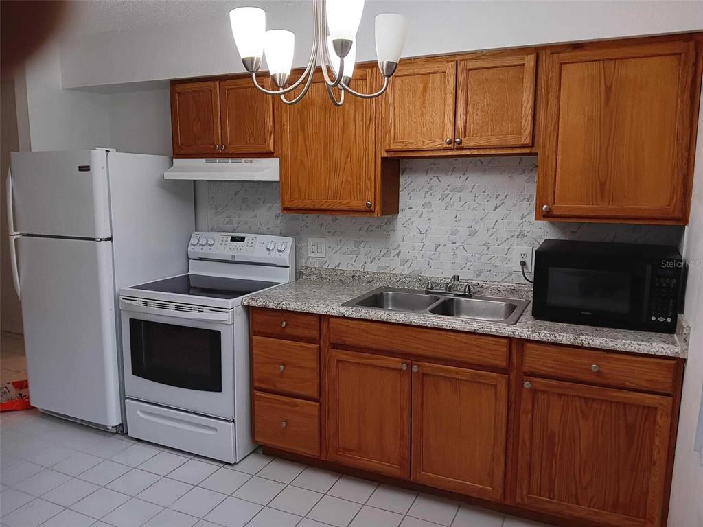 A kitchen features wood cabinets, granite countertops, white appliances, and a tiled floor — 714 MICHIGAN COURT UNIT 4, ST CLOUD, FL