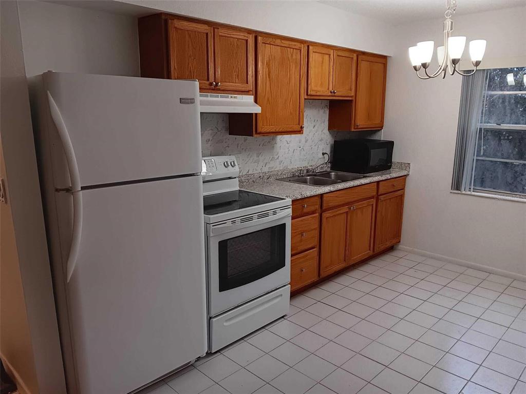 A kitchen features white appliances, wood cabinetry, a tiled floor, and a double-basin sink — 714 MICHIGAN COURT UNIT 4, ST CLOUD, FL