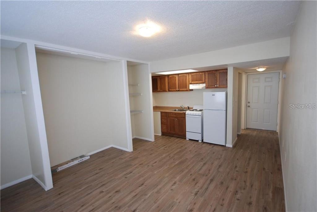 A studio apartment features wood-look flooring, a kitchenette with wooden cabinets, and a white refrigerator — 1254 E 113TH AVENUE UNIT C115, TAMPA, FL