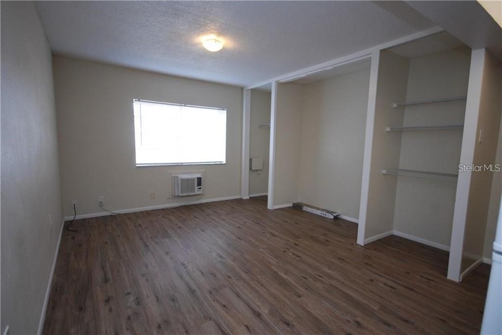 An empty room with wood-look flooring, a window air conditioner, and built-in shelving units — 1254 E 113TH AVENUE UNIT C115, TAMPA, FL