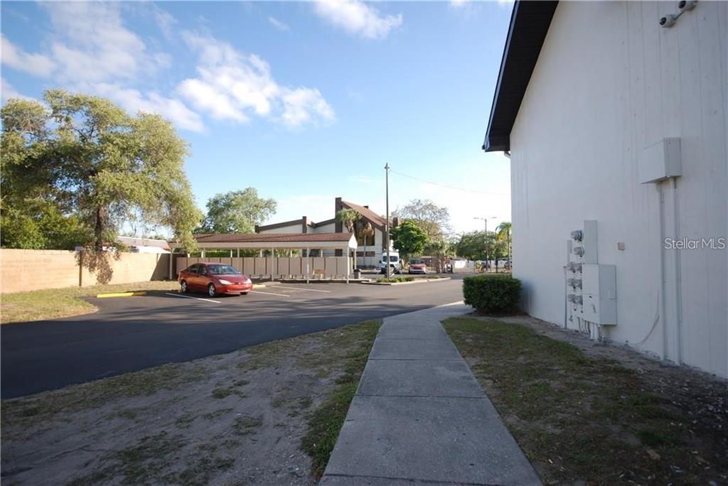 A paved walkway leads past a white building toward a parking lot with covered spaces — 1254 E 113TH AVENUE UNIT C115, TAMPA, FL