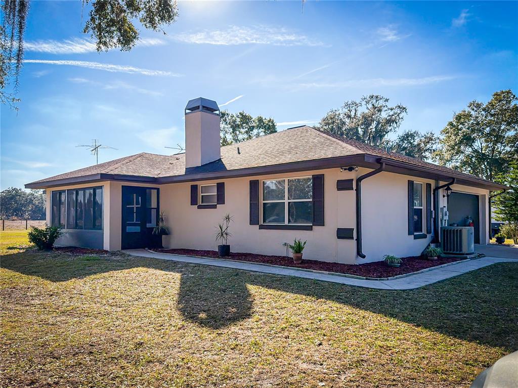 A single-story house with a chimney, dark shutters, and a screened-in porch under a blue sky — 1199 CR 542G, BUSHNELL, FL