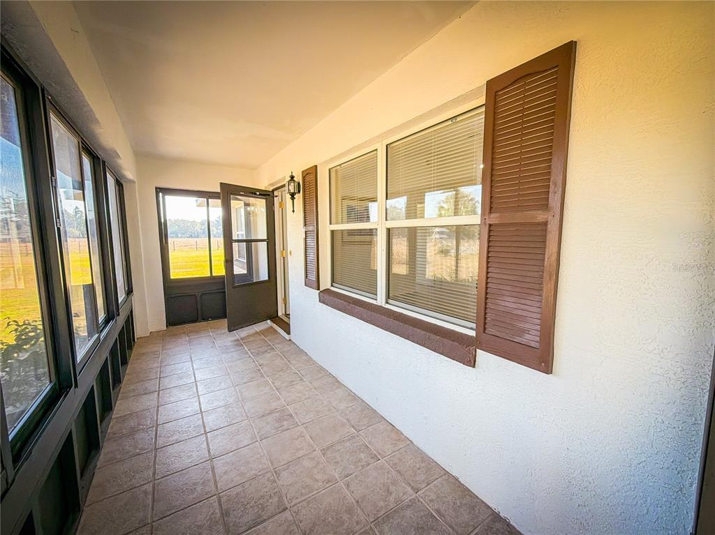 A tiled sunroom features a screen door, large windows with brown shutters, and white walls — 1199 CR 542G, BUSHNELL, FL