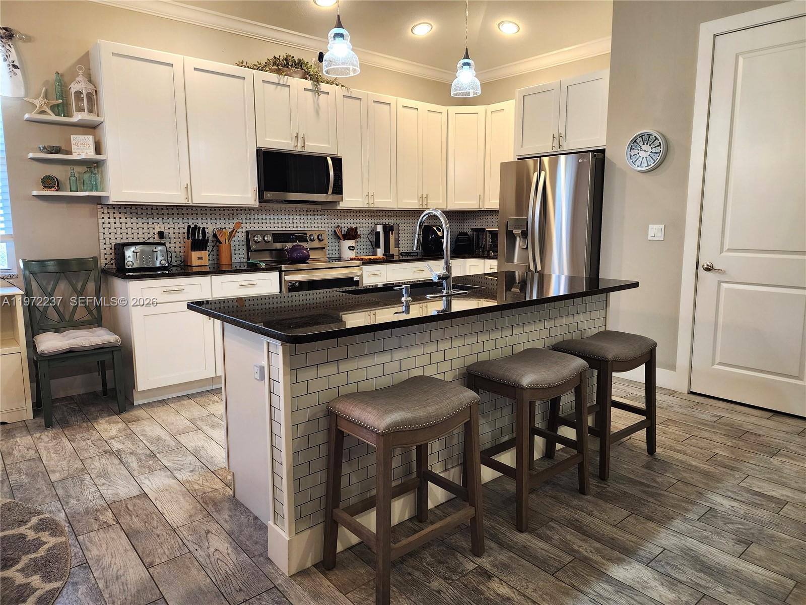 A kitchen features white cabinets, black countertops, a tiled island with bar stools, and stainless appliances — 108 Oak Knolls Circle, Sebring FL 33876, SEBRING, FL