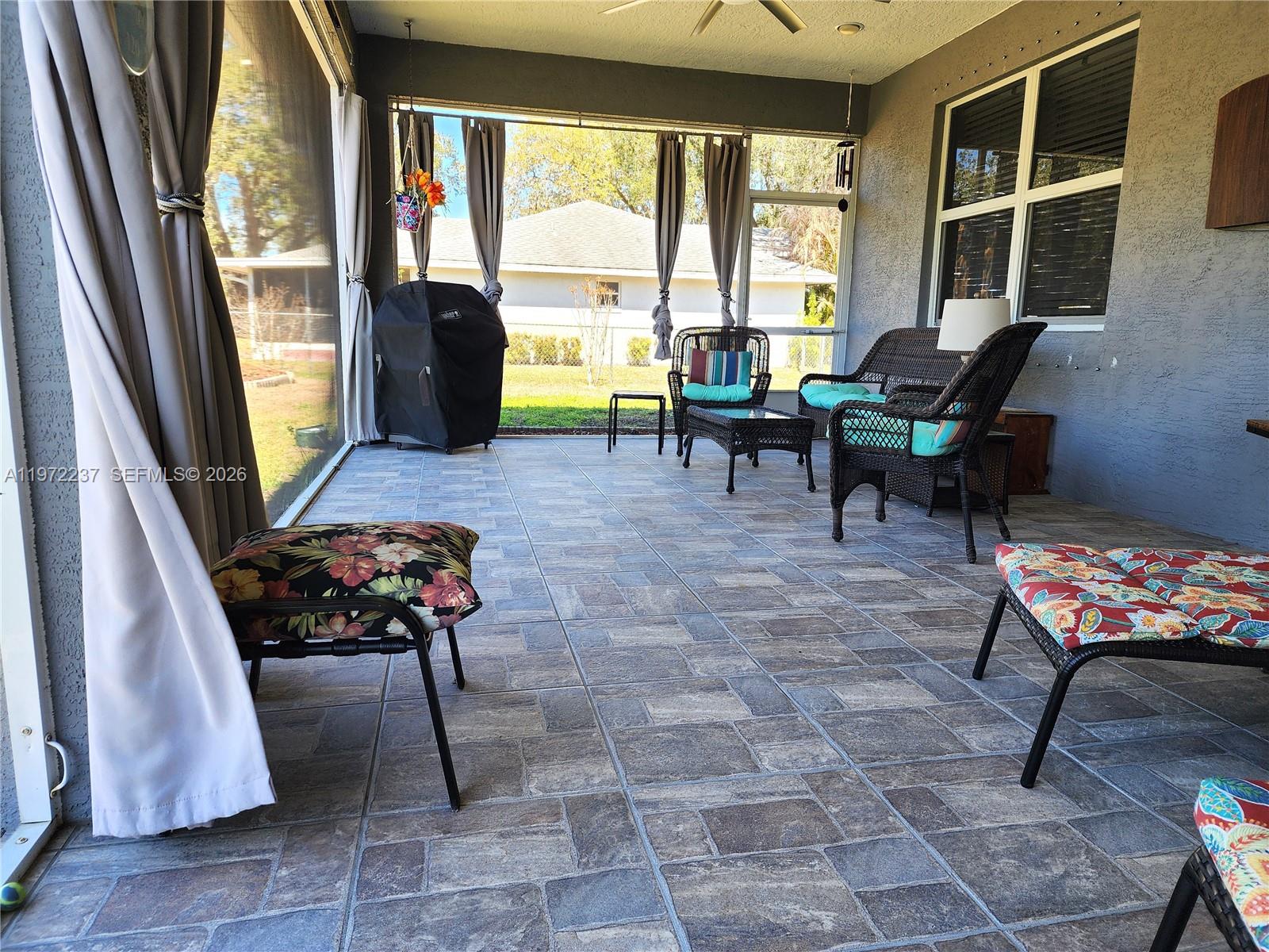 A screened-in patio features tiled flooring, wicker furniture, and a grill overlooking a backyard — 108 Oak Knolls Circle, Sebring FL 33876, SEBRING, FL