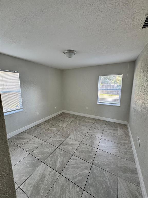 An empty room features light gray walls, white trim, and large square gray tile flooring — 1112 MARTIN STREET UNIT C, HAINES CITY, FL
