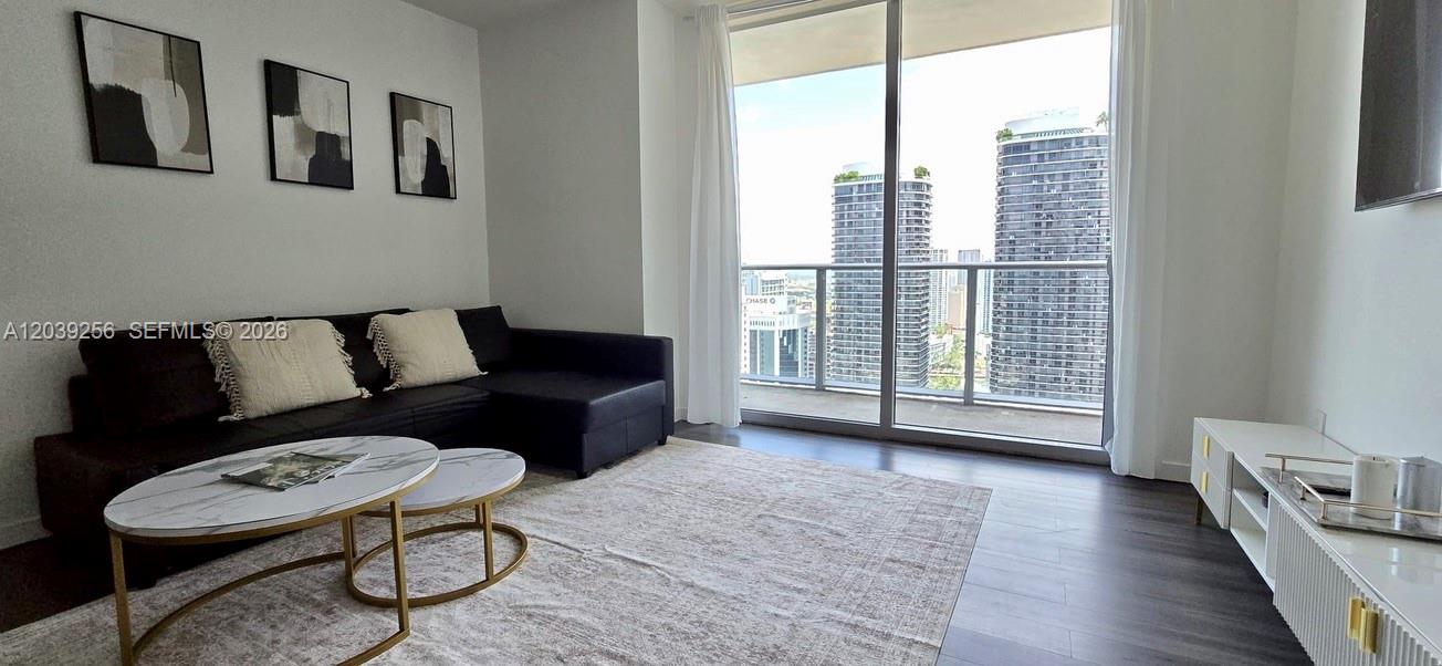 A modern living room features a black sectional sofa, marble coffee tables, and a balcony view — 1100 S Miami Ave # 3808, Miami FL 33130, MIAMI, FL