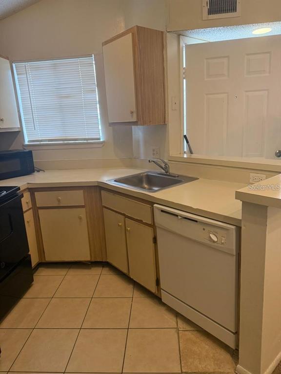 A kitchen features light-colored cabinets, a stainless steel sink, a white dishwasher, and tile flooring — 1972 LAKE ATRIUMS CIRCLE UNIT 187, ORLANDO, FL