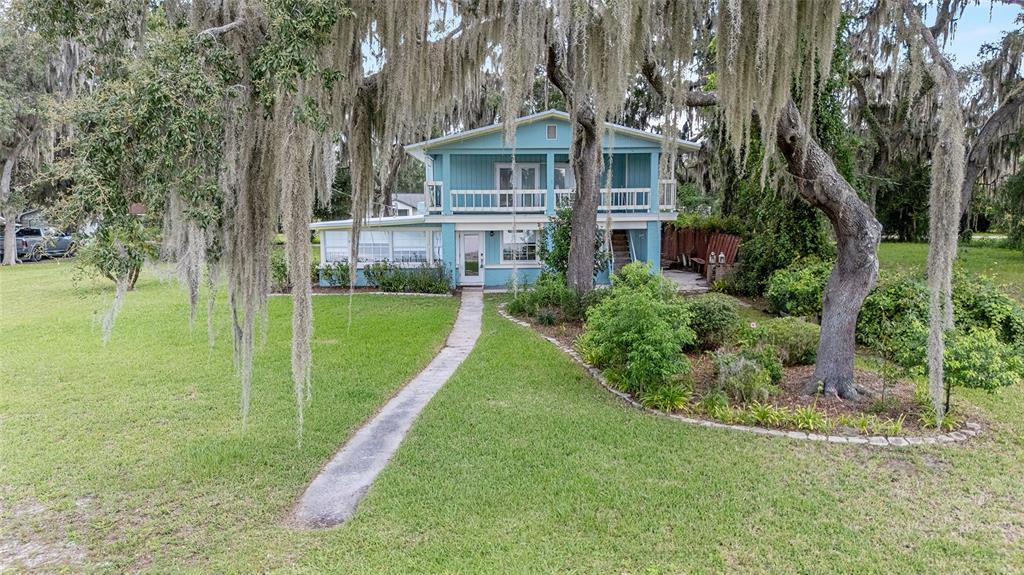 A two-story blue house with a balcony and a concrete walkway surrounded by large trees — 10399 NE 218TH LANE ROAD, FORT MC COY, FL