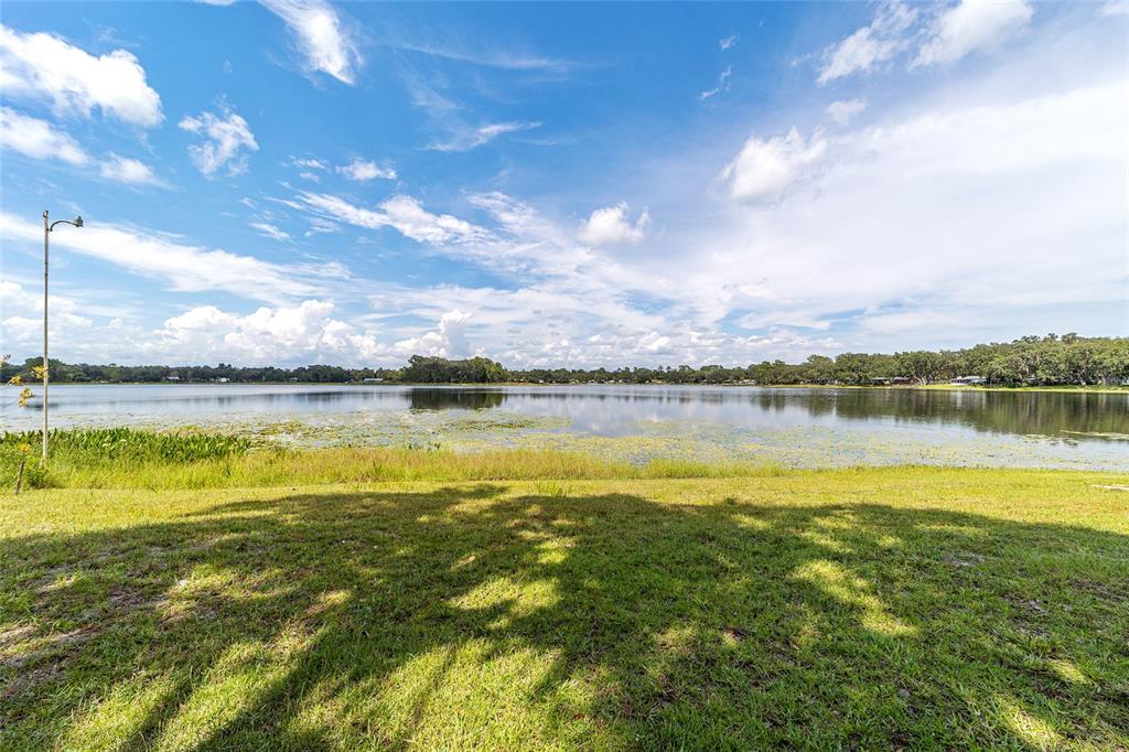 A grassy lawn overlooks a calm lake under a bright, partly cloudy blue sky — 10399 NE 218TH LANE ROAD, FORT MC COY, FL