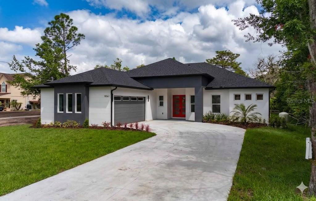 A modern single-story house with a gray and white exterior, a red door, and a driveway — 18561 SABAL STREET, ORLANDO, FL