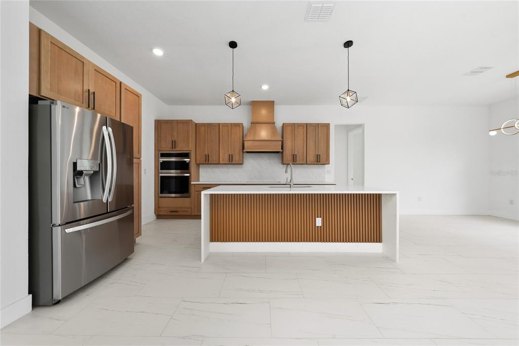 A modern kitchen features wood cabinets, a white island with slatted detail, and stainless appliances — 18561 SABAL STREET, ORLANDO, FL