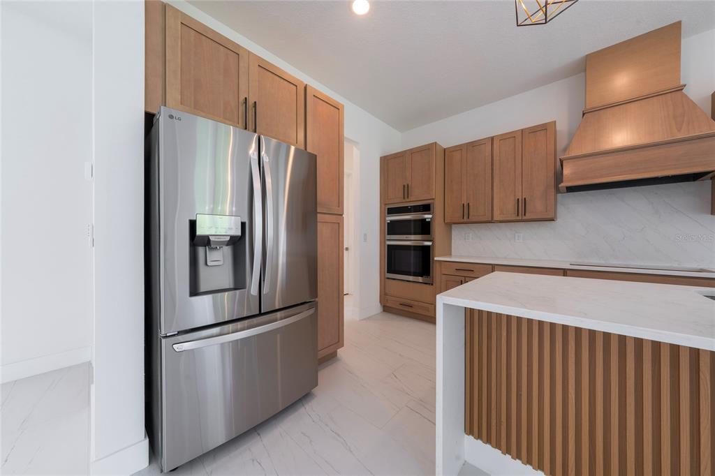 A modern kitchen features wood cabinets, stainless steel appliances, and a white marble-topped island — 18561 SABAL STREET, ORLANDO, FL