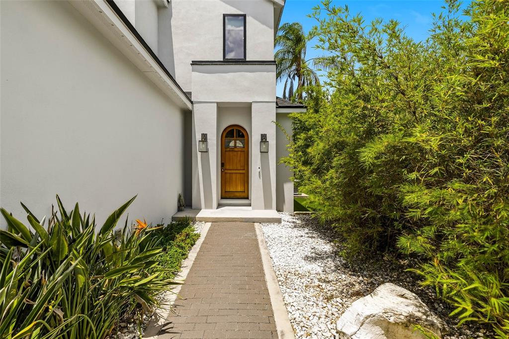 A paved walkway leads to a wooden arched front door of a white modern house — 723 SYMONDS AVENUE, WINTER PARK, FL