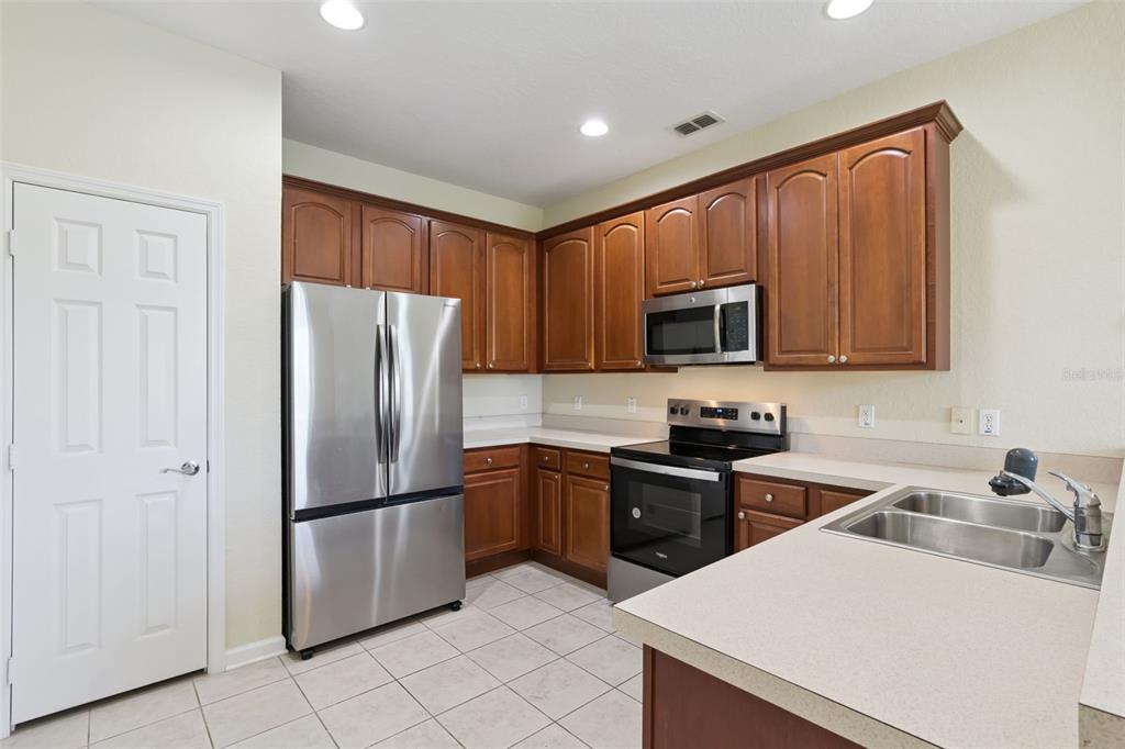 A kitchen with wood cabinets, stainless steel appliances, tile flooring, and light-colored countertops — 1431 SHALLCROSS AVENUE, ORLANDO, FL