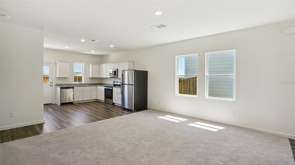 A kitchen with white cabinets and stainless steel appliances opens into a carpeted living area — 1640 NORFOLK TRAIL, DELAND, FL