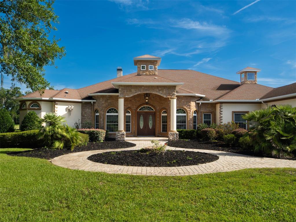 A stone-facade house with a circular driveway, arched entryway, and a cupola under blue skies — 6853 NW 12TH STREET, OCALA, FL
