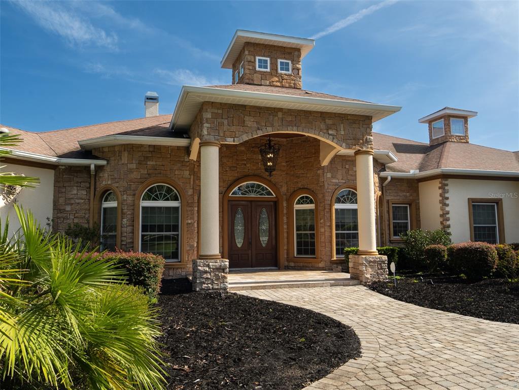 The exterior of a stone-faced house features a covered entryway with columns and a cupola — 6853 NW 12TH STREET, OCALA, FL