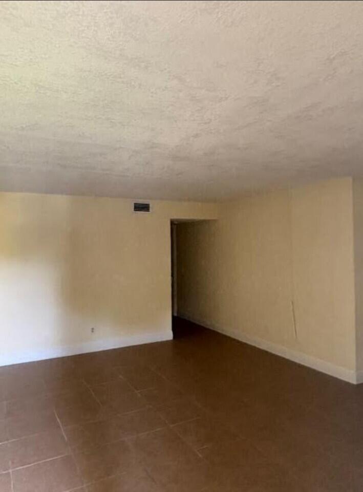 An empty room with beige walls, brown tile flooring, and a doorway leading to darkness — 1205 Meadows Circle, Boynton Beach FL 33436, BOYNTON BEACH, FL