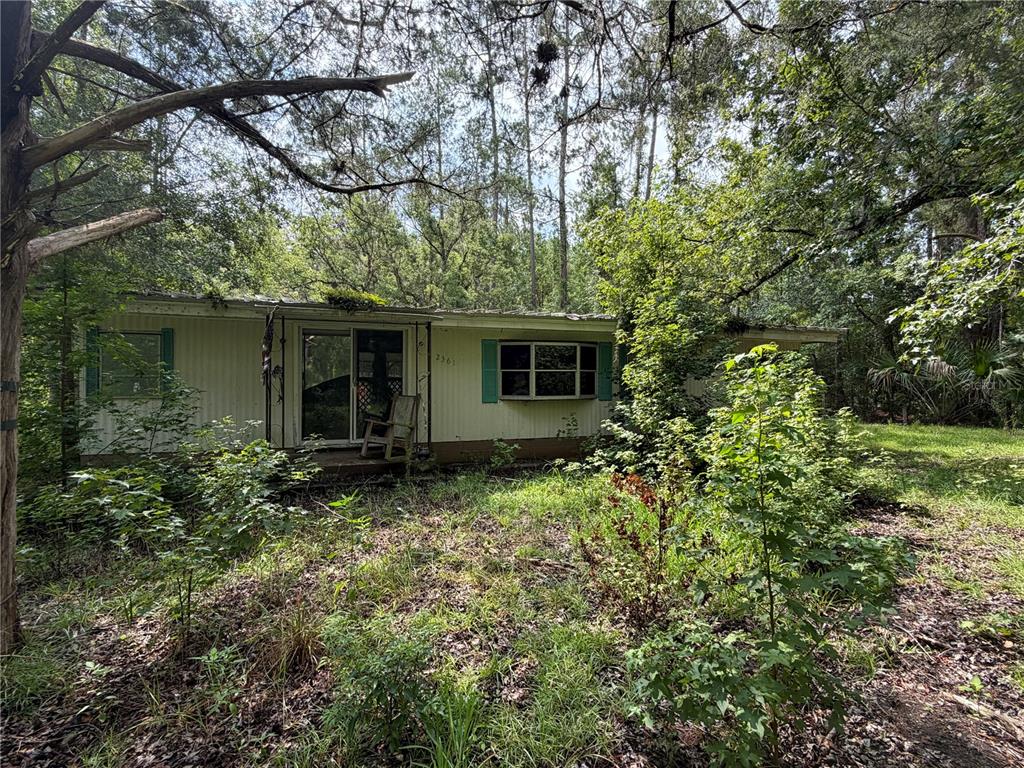 A single-story mobile home sits behind a chain-link fence in a wooded, grassy lot — 2361 NE 115TH AVENUE, SILVER SPRINGS, FL