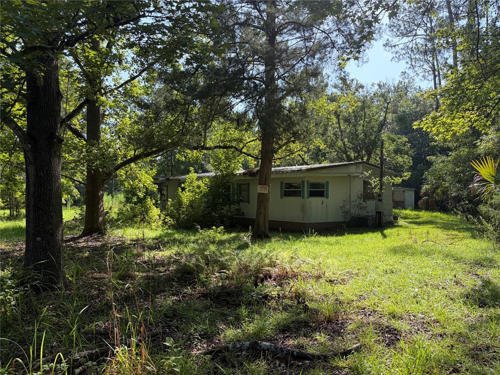 A weathered, single-story mobile home sits in a wooded lot with overgrown vegetation — 2361 NE 115TH AVENUE, SILVER SPRINGS, FL