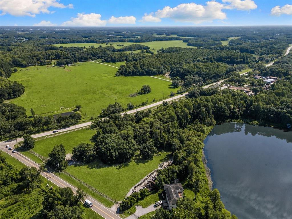 An aerial view shows a house situated next to a lake, surrounded by green fields — 18117 BOY SCOUT ROAD, ODESSA, FL