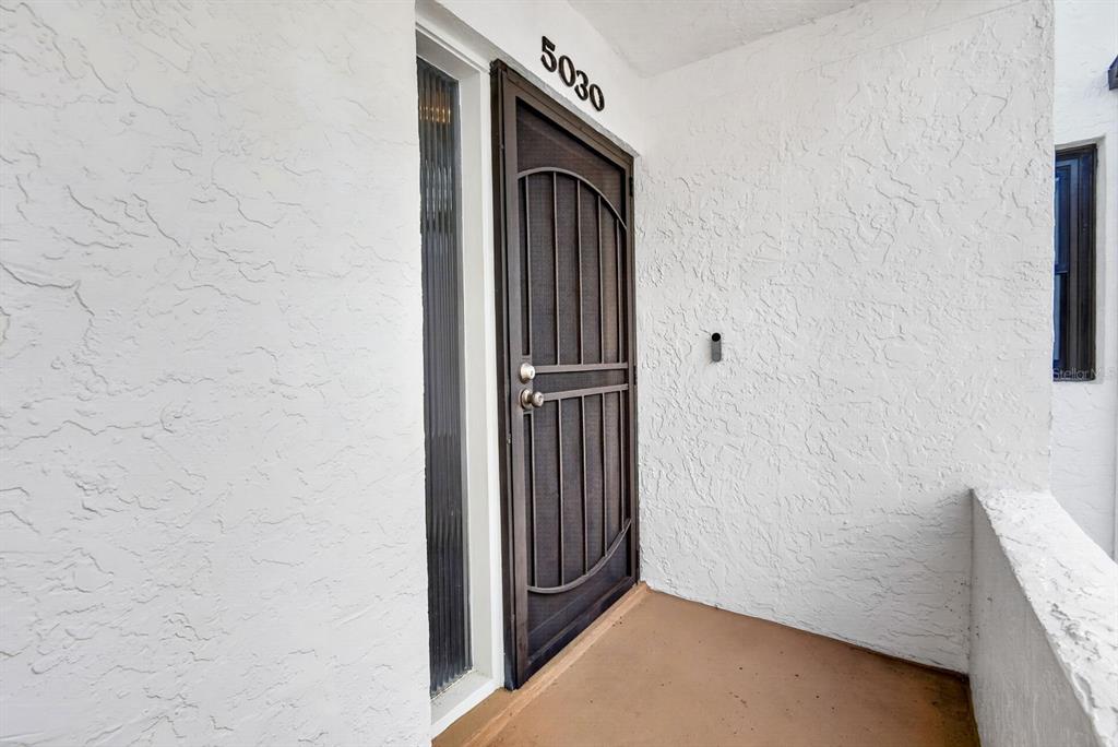 A brown screen door with a decorative arch sits on a porch with white walls — 5030 MARSH FIELD ROAD UNIT 22, SARASOTA, FL