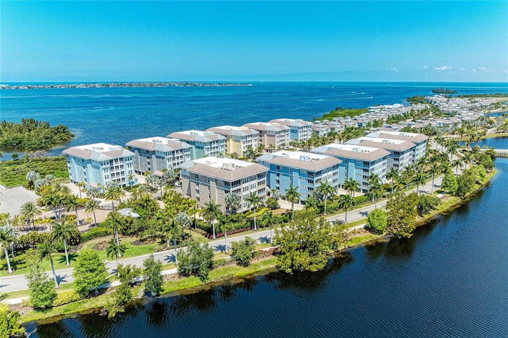 An aerial view of multi-story apartment buildings situated along a waterfront with palm trees — 395 ARUBA CIRCLE UNIT 402, BRADENTON, FL