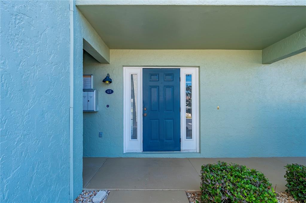 A blue front door with side windows is set into a light blue stucco exterior wall — 1400 MINEO DRIVE UNIT 12T, PUNTA GORDA, FL