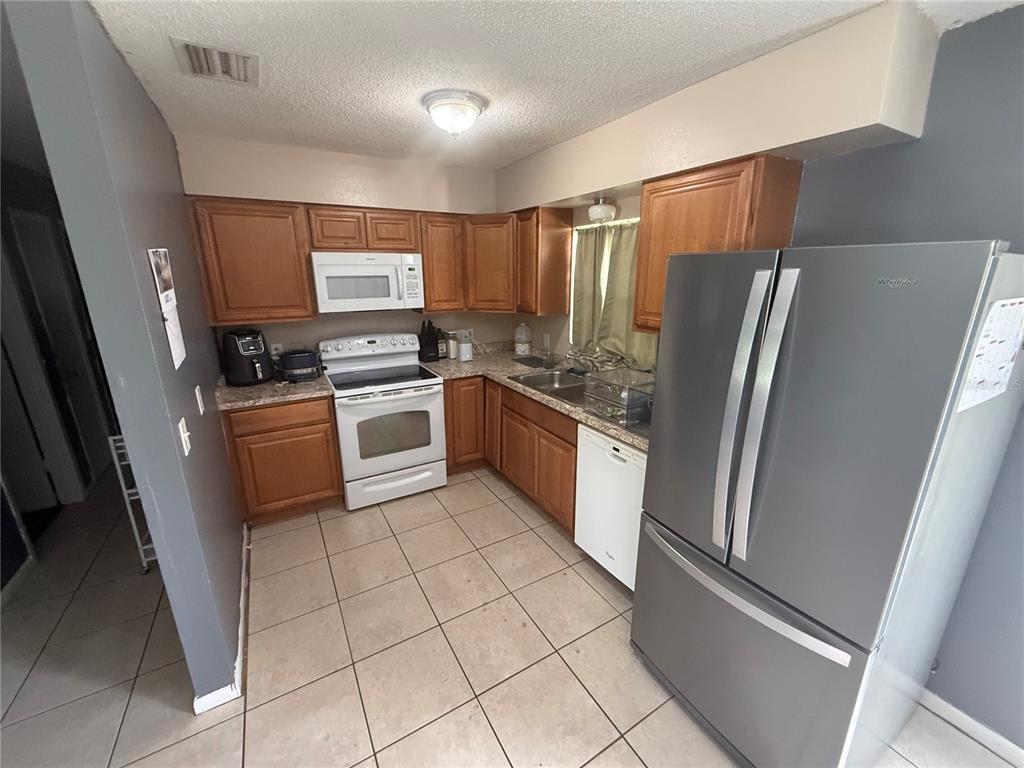 A kitchen features wood cabinets, tile flooring, and stainless steel appliances including a refrigerator — 11129 ROBERTS LANE, RIVERVIEW, FL