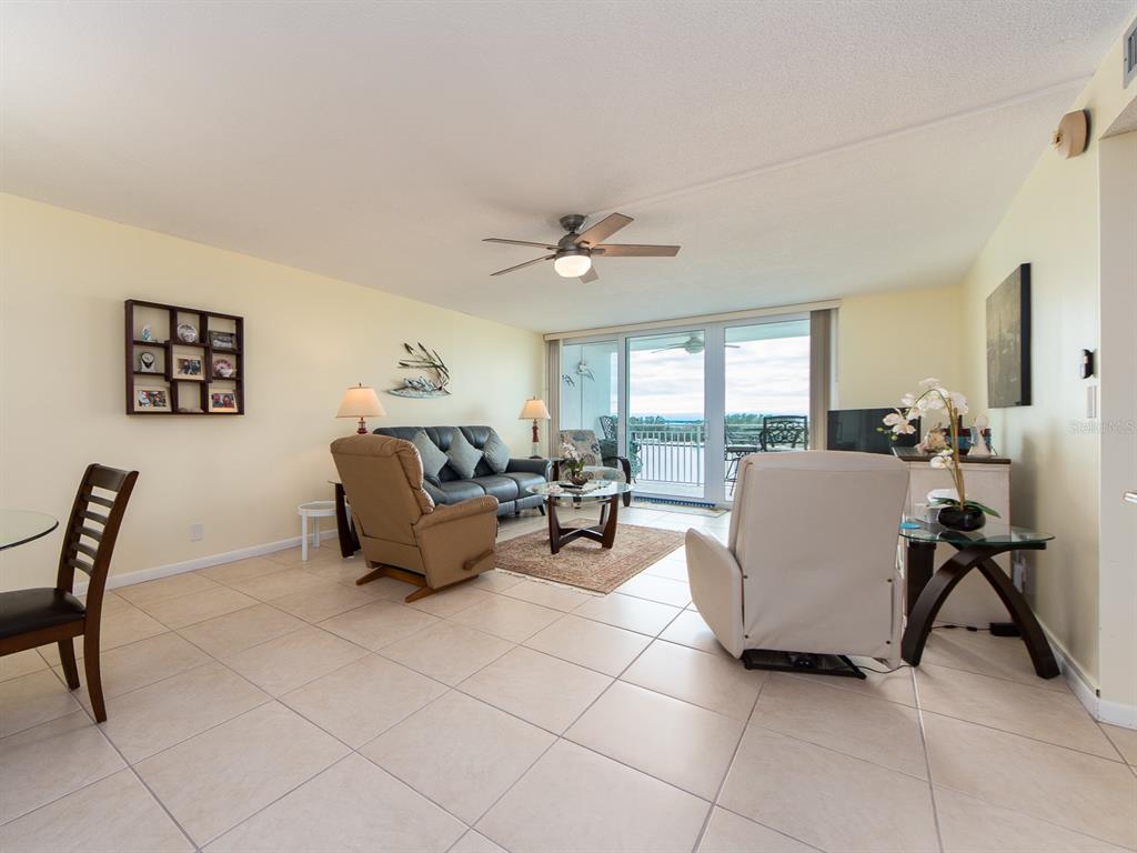 A living room with tile floors, a ceiling fan, and sliding glass doors to a balcony — 675 S GULFVIEW BOULEVARD UNIT 902, CLEARWATER BEACH, FL